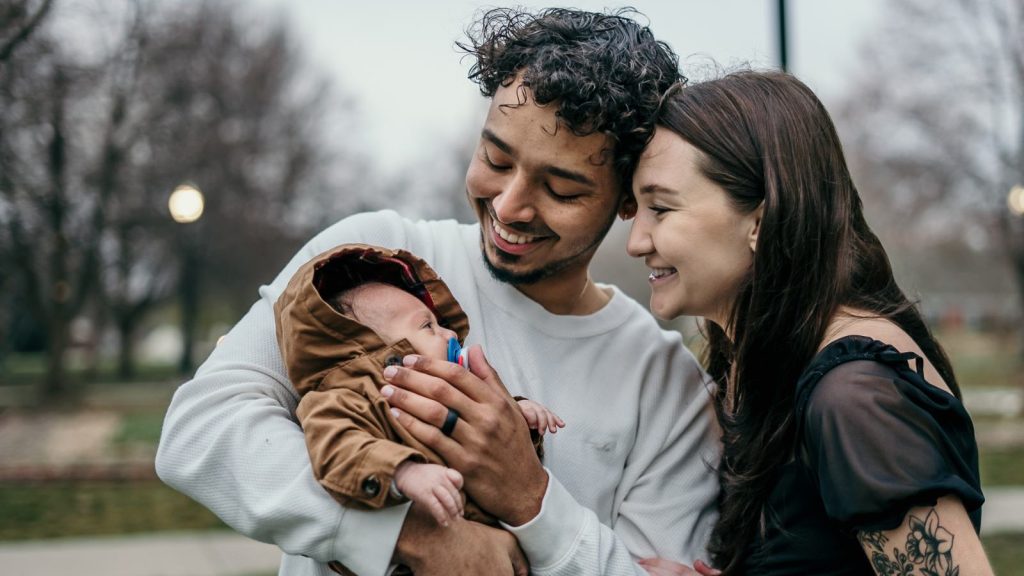 Parents smiling as they hold their newborn outdoors
